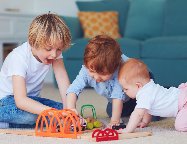 3 kids aged 1 - 5 years old playing together with toys.